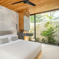 Open-concept bedroom with a tropical palm wallpaper accent wall, wood ceiling, and glass doors overlooking a private garden.