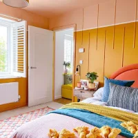 Colorful dopamine decor bedroom with mustard yellow paneled walls, a coral upholstered headboard, teal pillows, and vibrant patterned textiles.