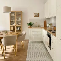 Small white kitchen with wood countertops, glass-front cabinet, dining table, and patterned floor tile