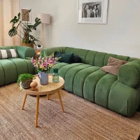 Green curved sectional sofa with striped pillows, a round wooden coffee table, plants, and floral decor in a cozy living room.