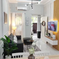 Small living room with a compact gray sofa, round coffee table, wall-mounted TV, white furniture, and natural wood accents.