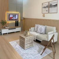 Warm neutral living room with a cream sofa, wood paneling, patterned rug, framed artwork, and a woven coffee table.