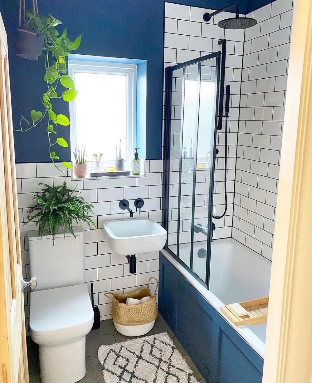 small bathroom with white subway tile walls, navy blue accents, a wall-mounted sink, and a glass shower enclosure