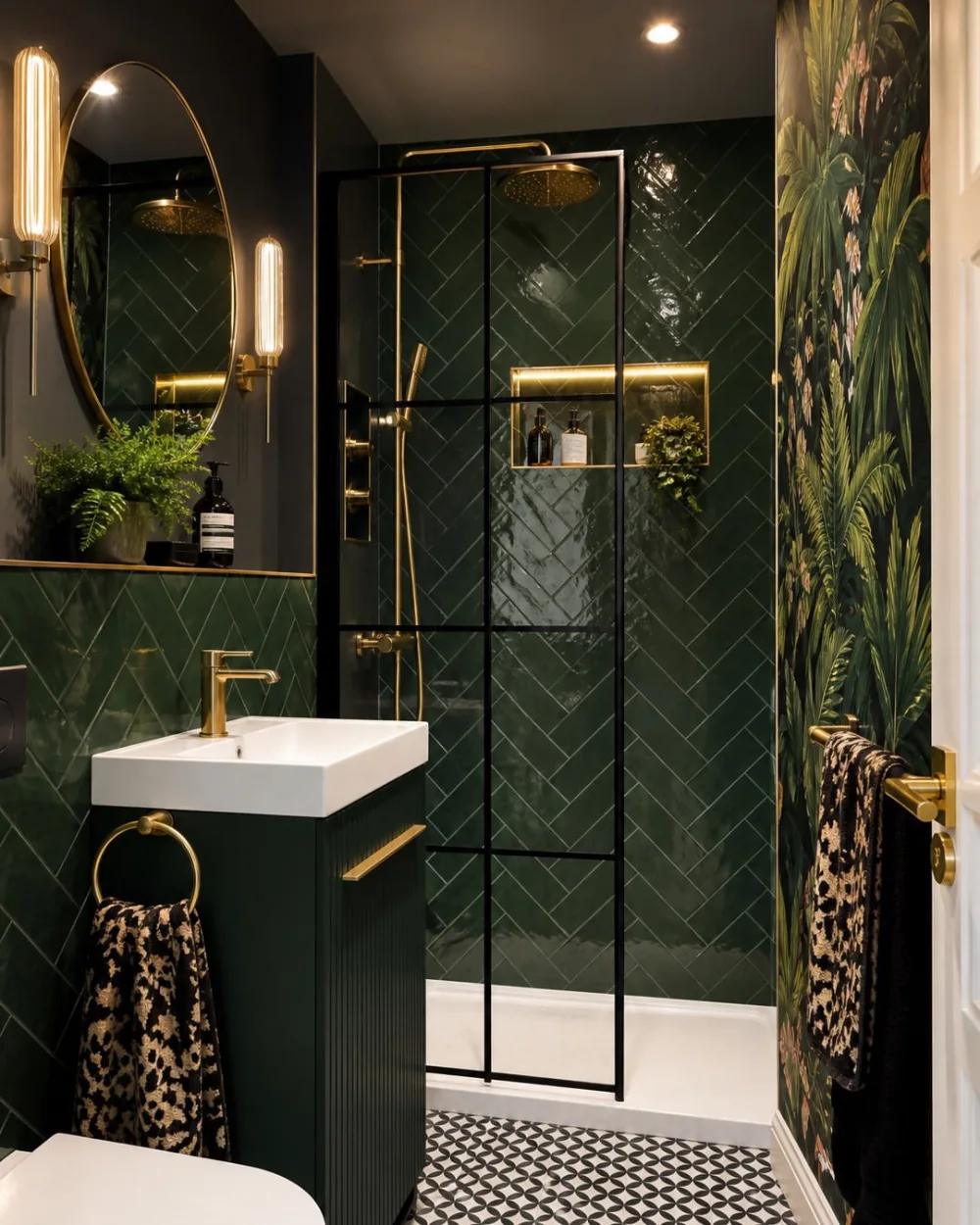 small dark green bathroom with herringbone tile, black shower enclosure, gold fixtures, and botanical wallpaper