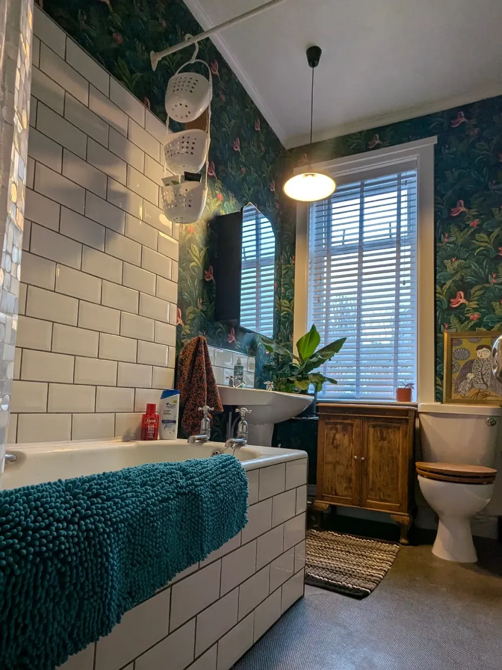 small bathroom with dark botanical wallpaper, white subway tile around the bathtub, and a vintage wooden cabinet
