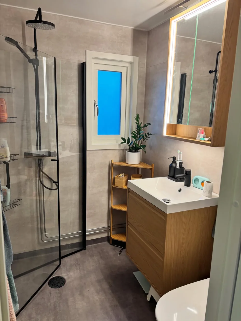 small bathroom with blue-gray herringbone shower tiles, frameless glass enclosure, and floating wood vanity