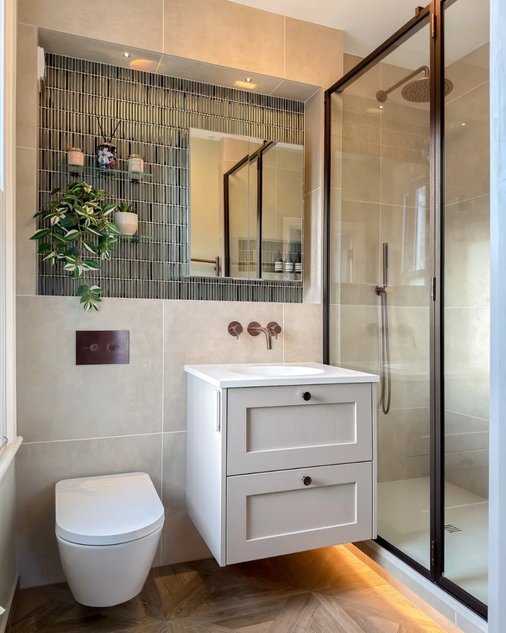 small bathroom with green tiled shower, floating white vanity, round mirror, and recessed wall shelves