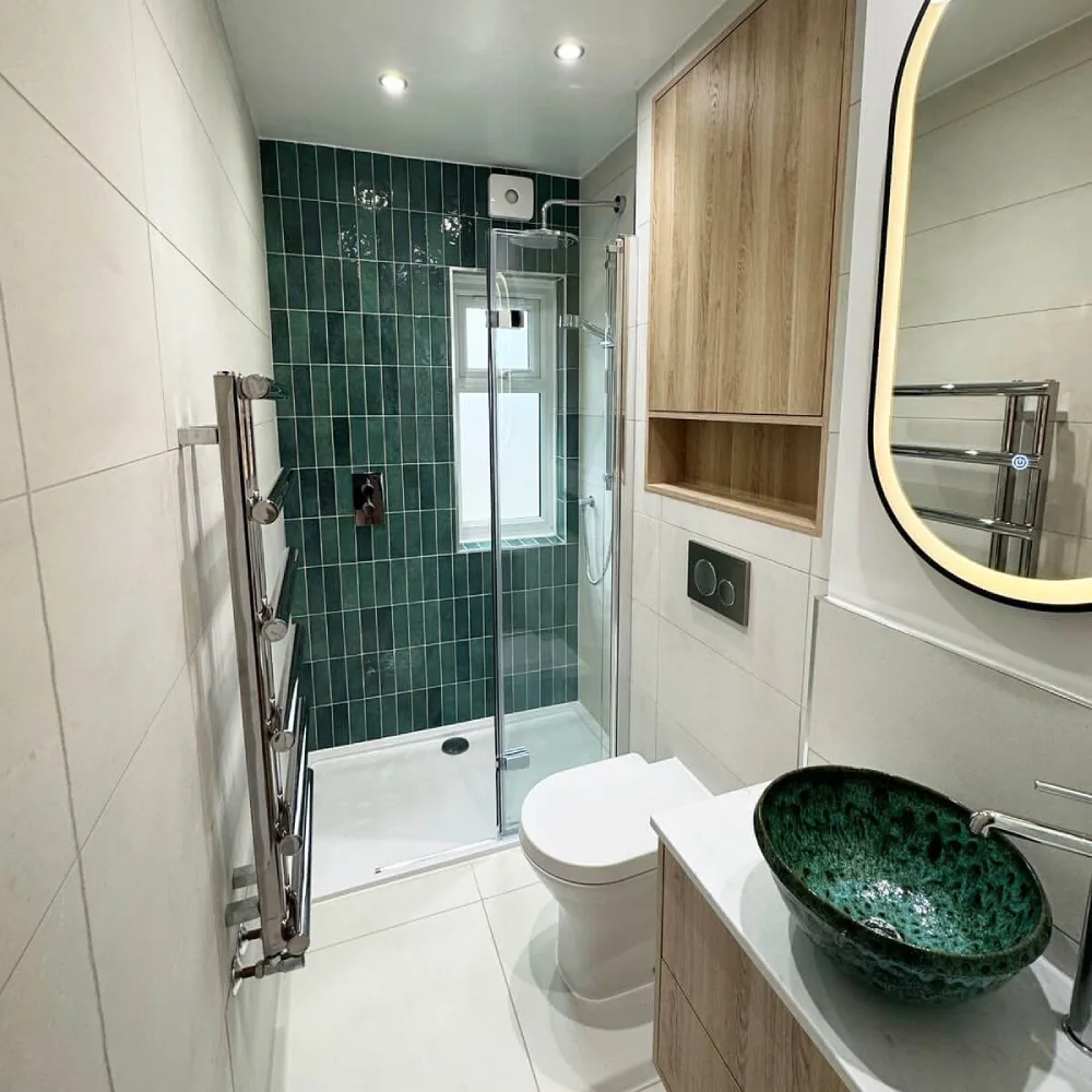 narrow bathroom with dark green vertical shower tiles, wood storage cabinet, and compact wood vanity