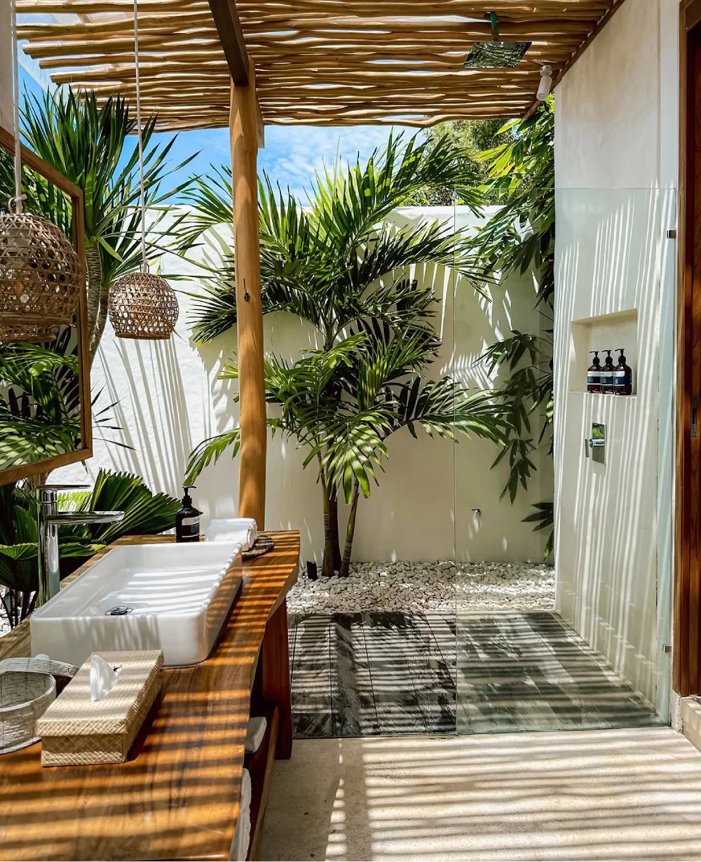 open-concept bathroom with a glass shower, tropical garden, wooden vanity, and pergola roof