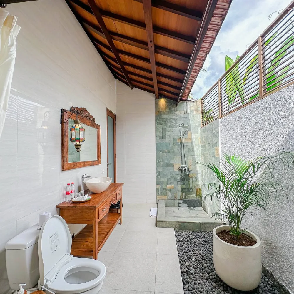 semi-outdoor bathroom with stone shower, wooden vanity, tropical plant, and open roof section