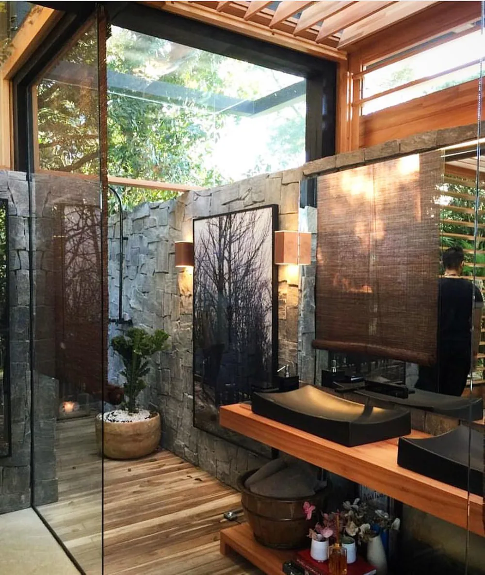 open bathroom with glass doors, stone walls, wood vanity, and tropical garden beyond