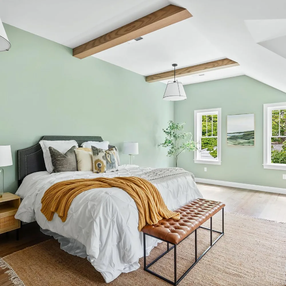 light green bedroom with wood ceiling beams, dark headboard, and warm accents