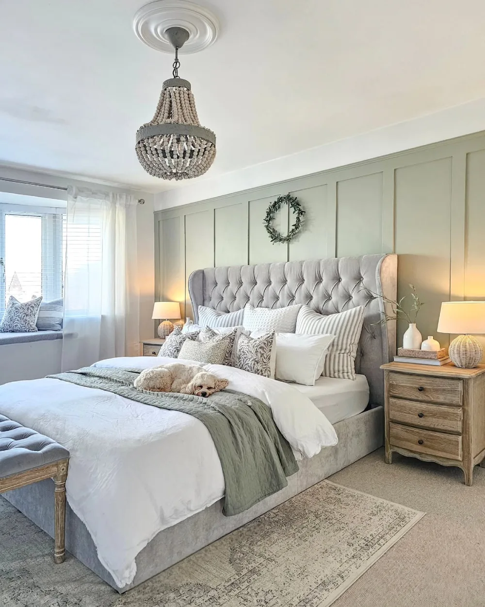 soft green bedroom with tufted headboard, layered neutral bedding, and paneled wall
