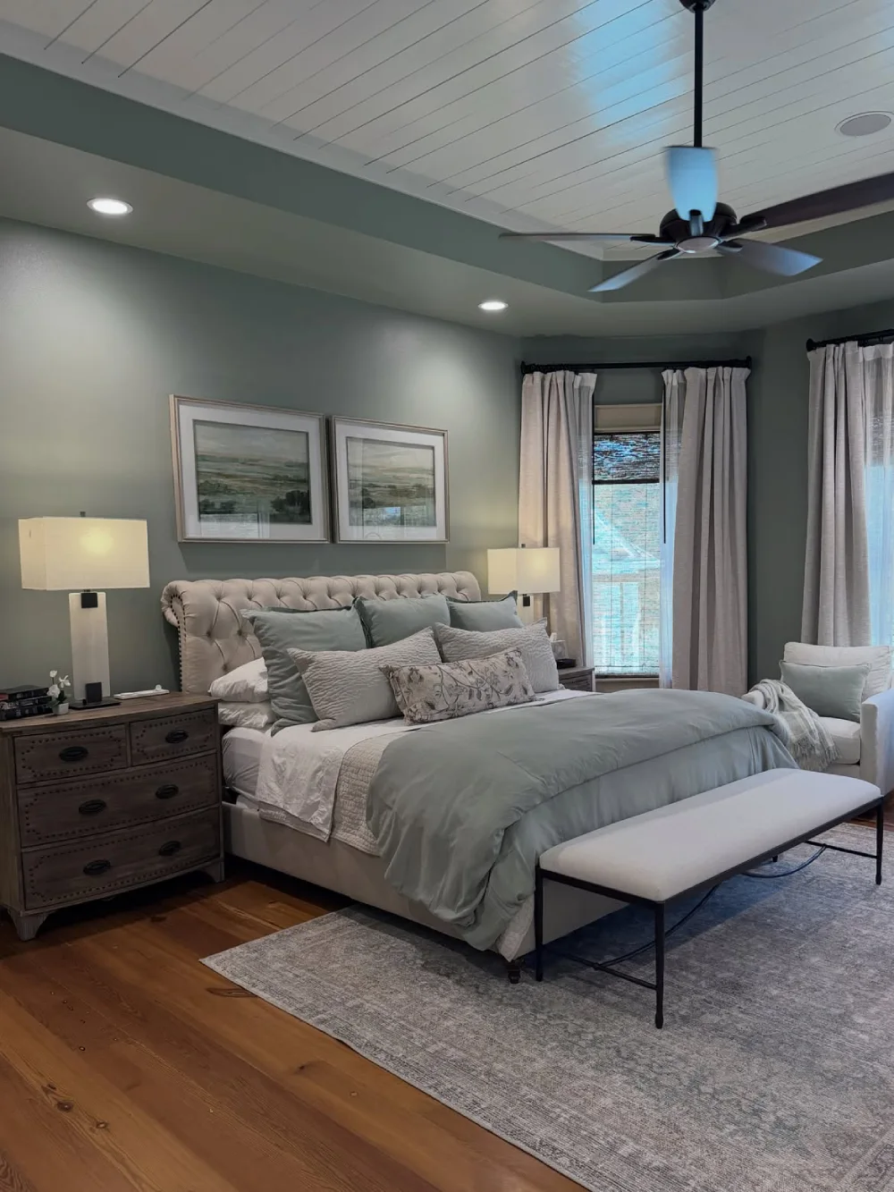 moody green bedroom with tufted headboard, neutral bedding, and wood furniture