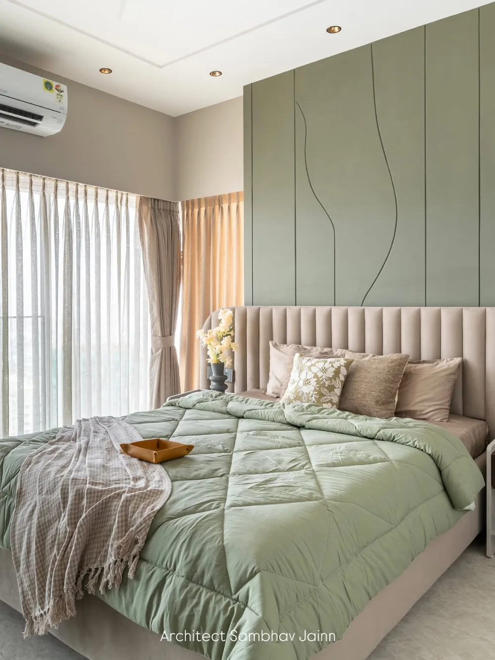 light green bedroom with upholstered bed, layered bedding, and large windows