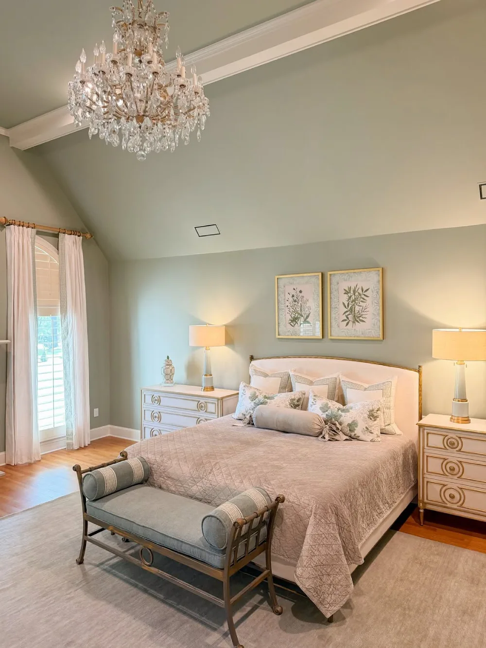 soft green bedroom with blush bedding, floral artwork, and crystal chandelier