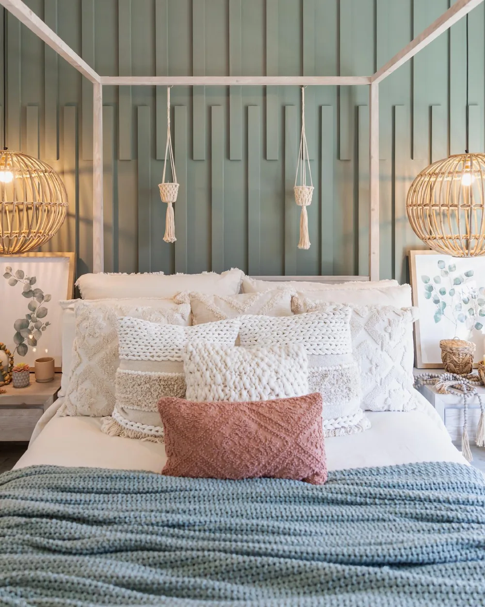 Cozy bedroom with a sage green vertical paneled accent wall, white canopy bed, woven pendant lights, textured cream pillows, and a dusty pink accent cushion