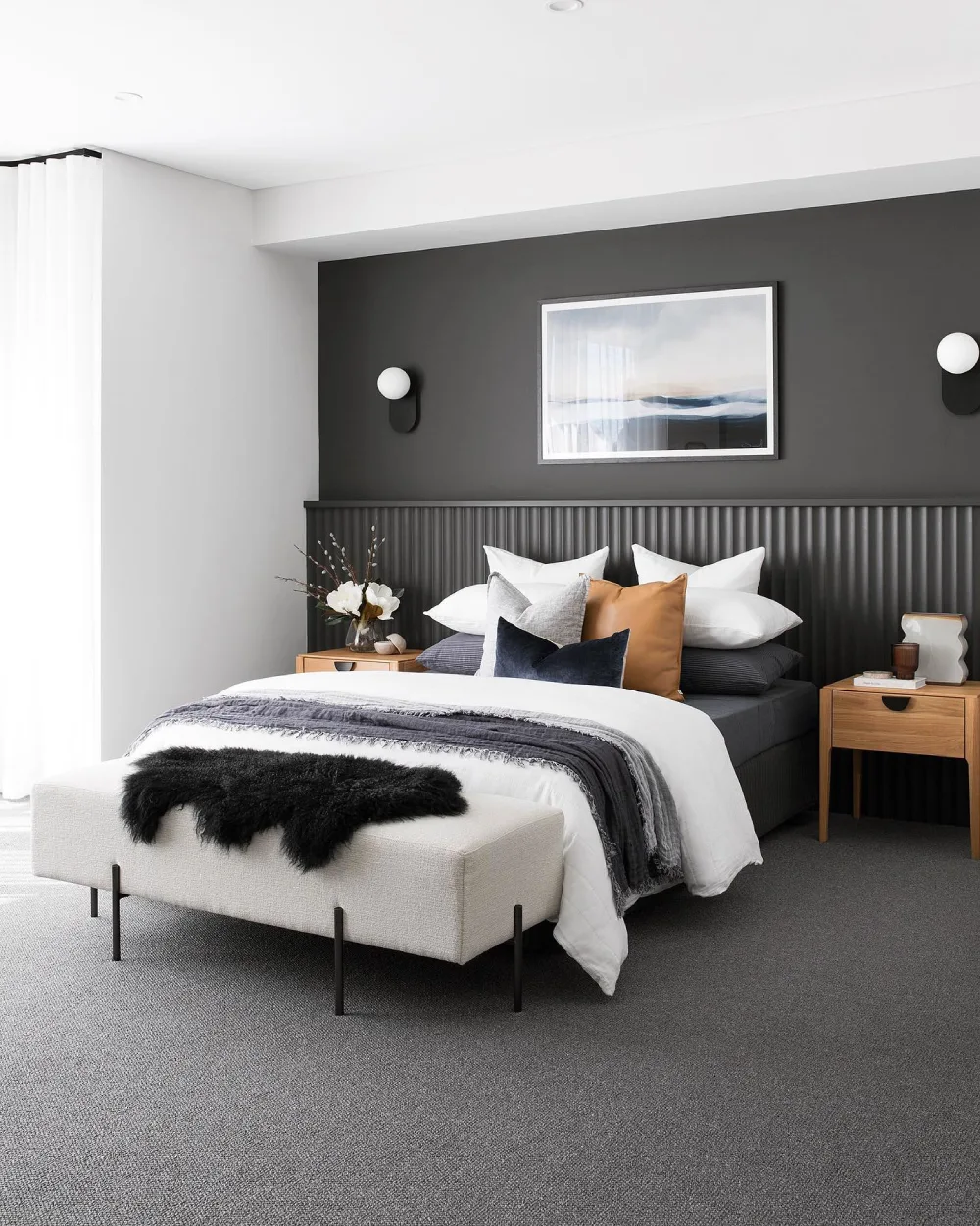 Modern bedroom with a charcoal accent wall, ribbed headboard, white bedding, and warm wood nightstands