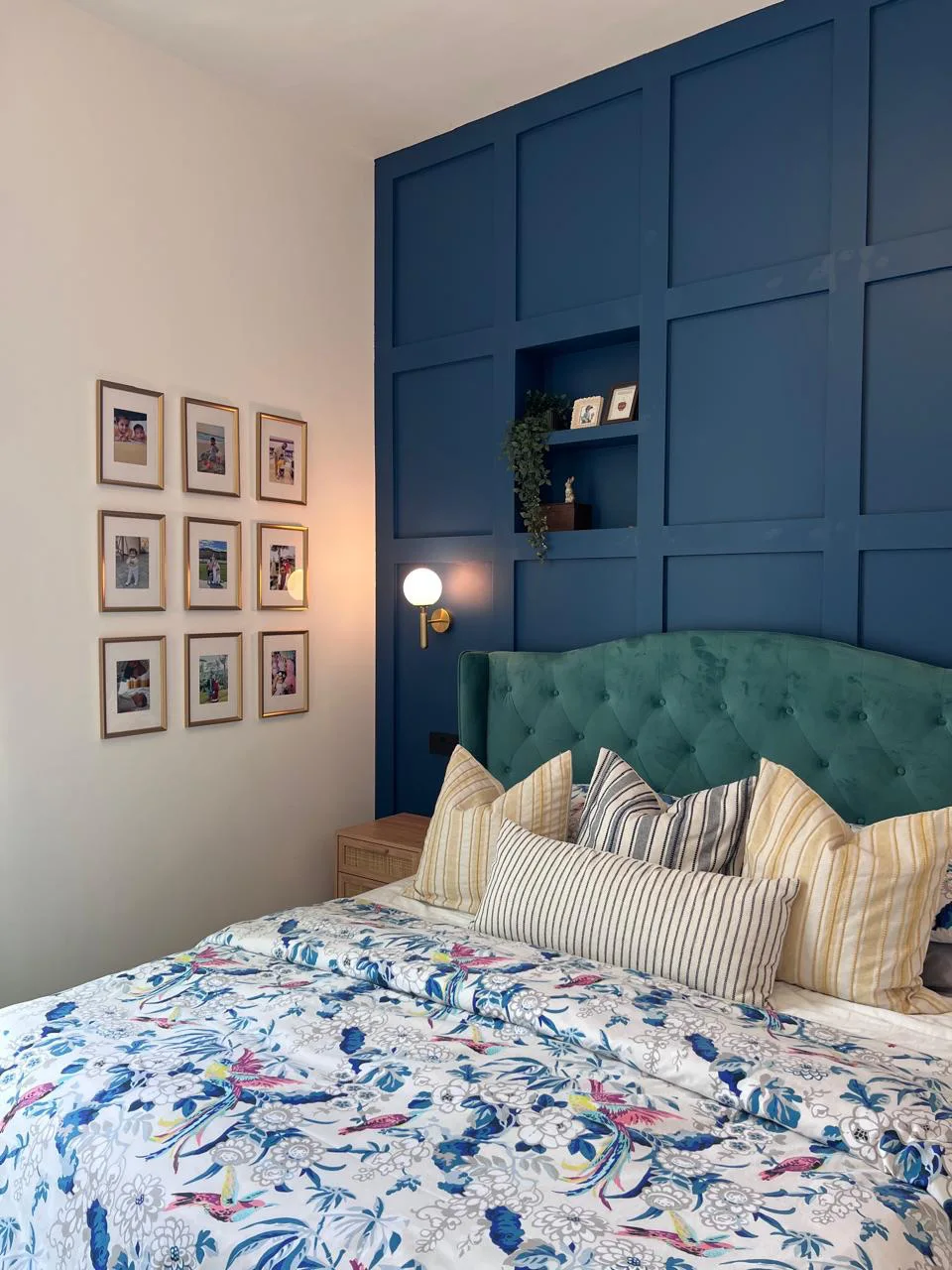 Bedroom with a deep blue paneled accent wall, green tufted headboard, brass wall sconce, and patterned bedding