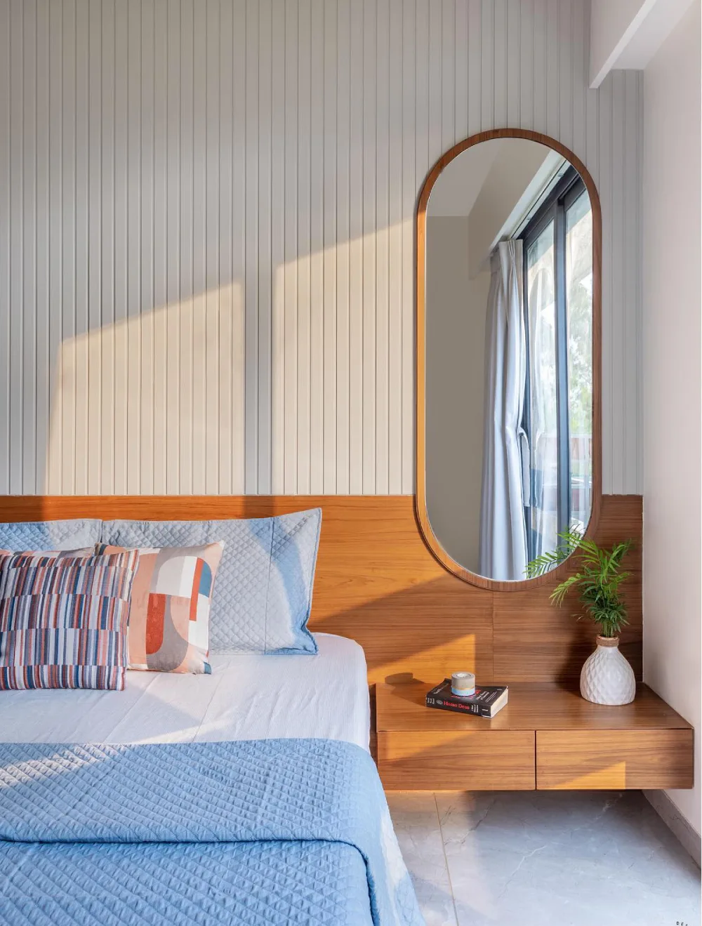 Bright bedroom with a vertical paneled wall, natural wood headboard, arched mirror, and floating wooden nightstand