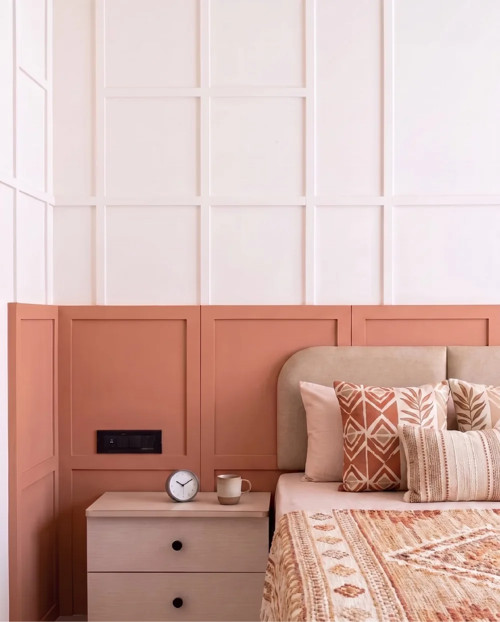 Warm bedroom with a terracotta paneled accent wall, beige upholstered headboard, and earthy decorative pillows