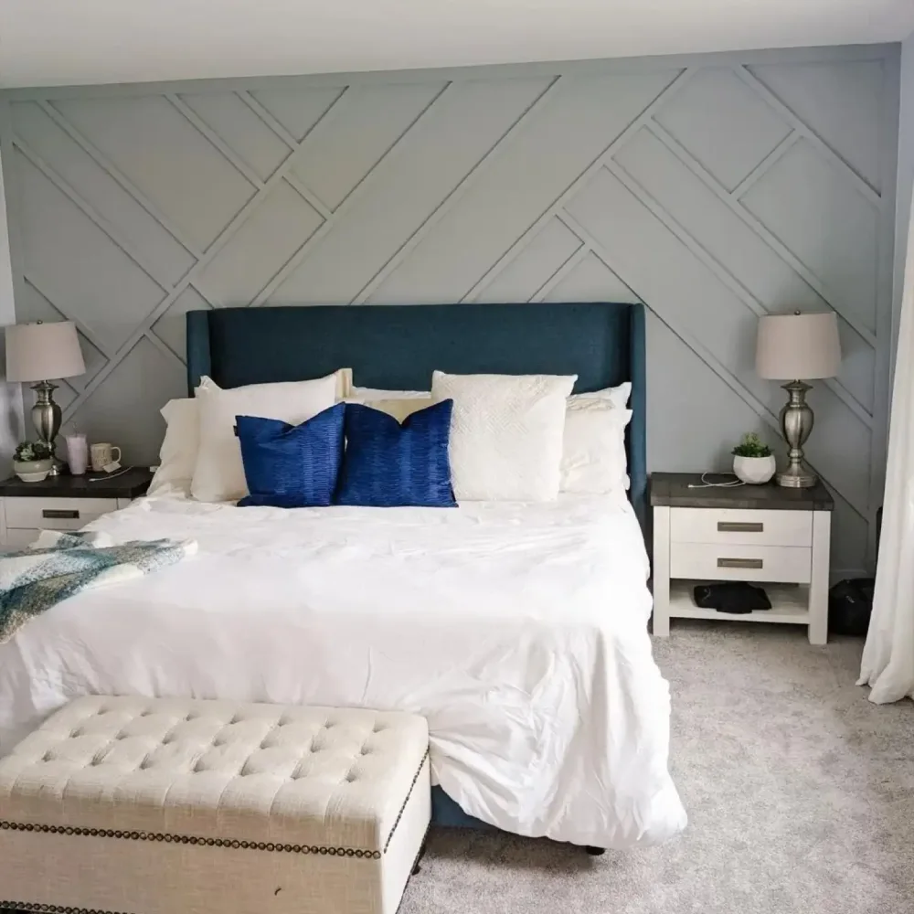 Gray geometric paneled bedroom accent wall with a dark teal upholstered headboard, white bedding, and bold blue pillows