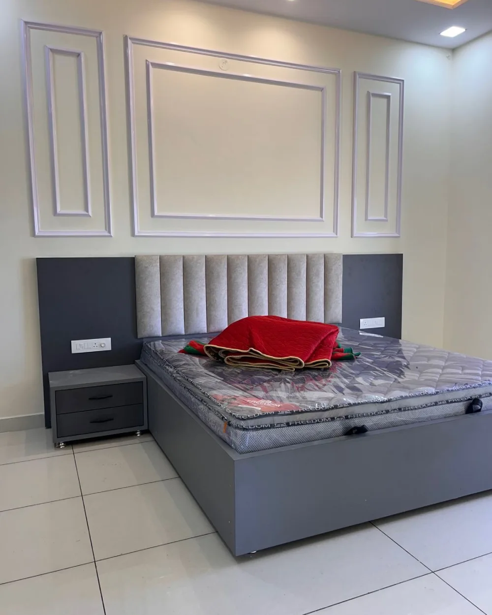 Modern bedroom featuring white decorative wall molding, charcoal accent panels behind a gray upholstered headboard, and a minimalist gray bed frame