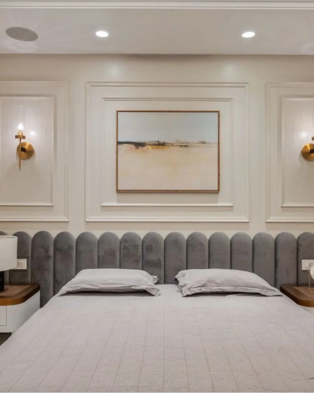 Contemporary bedroom with white decorative wall molding, a gray channel-tufted upholstered headboard, neutral bedding, and warm wooden bedside tables