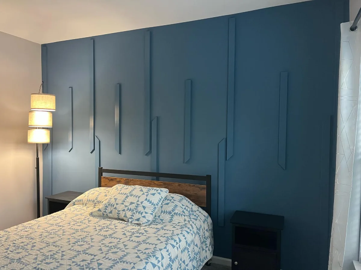 Bedroom with a navy blue accent wall featuring geometric wood trim, a rustic wooden headboard, and blue-and-white geometric bedding.