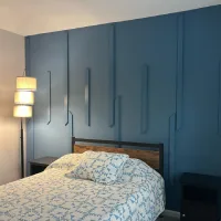 Bedroom with a navy blue accent wall featuring geometric wood trim, a rustic wooden headboard, and blue-and-white geometric bedding.