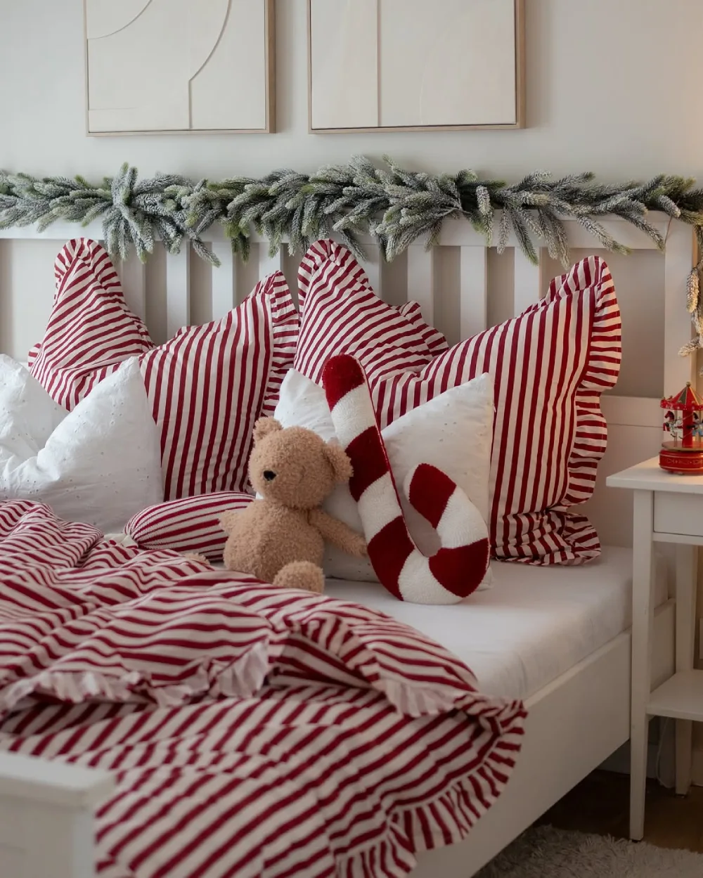 Cozy white bedroom with red and white striped bedding, candy cane pillow, and evergreen garland