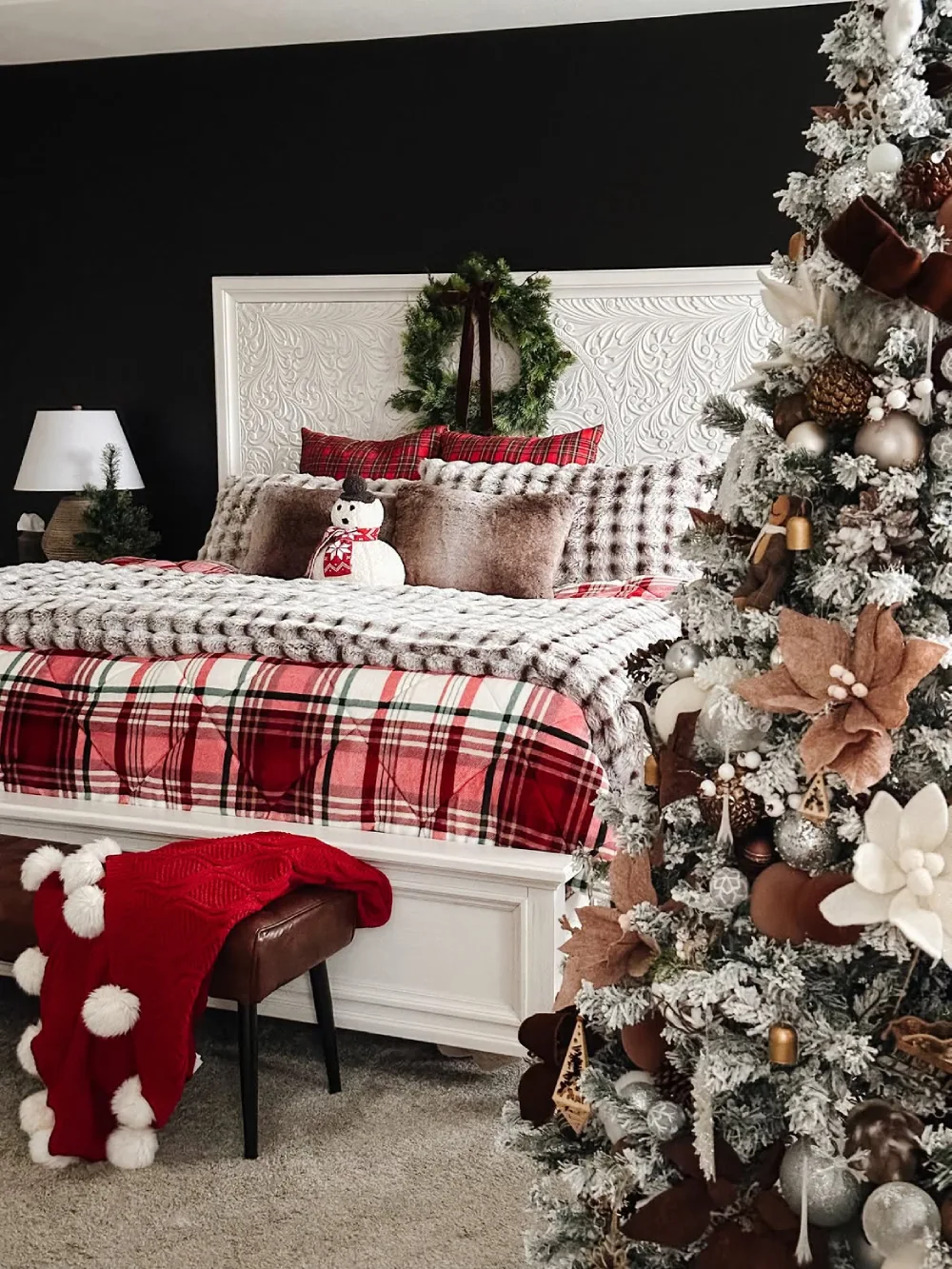 Winter bedroom with black accent wall, plaid bedding, chunky blankets, and a flocked Christmas tree