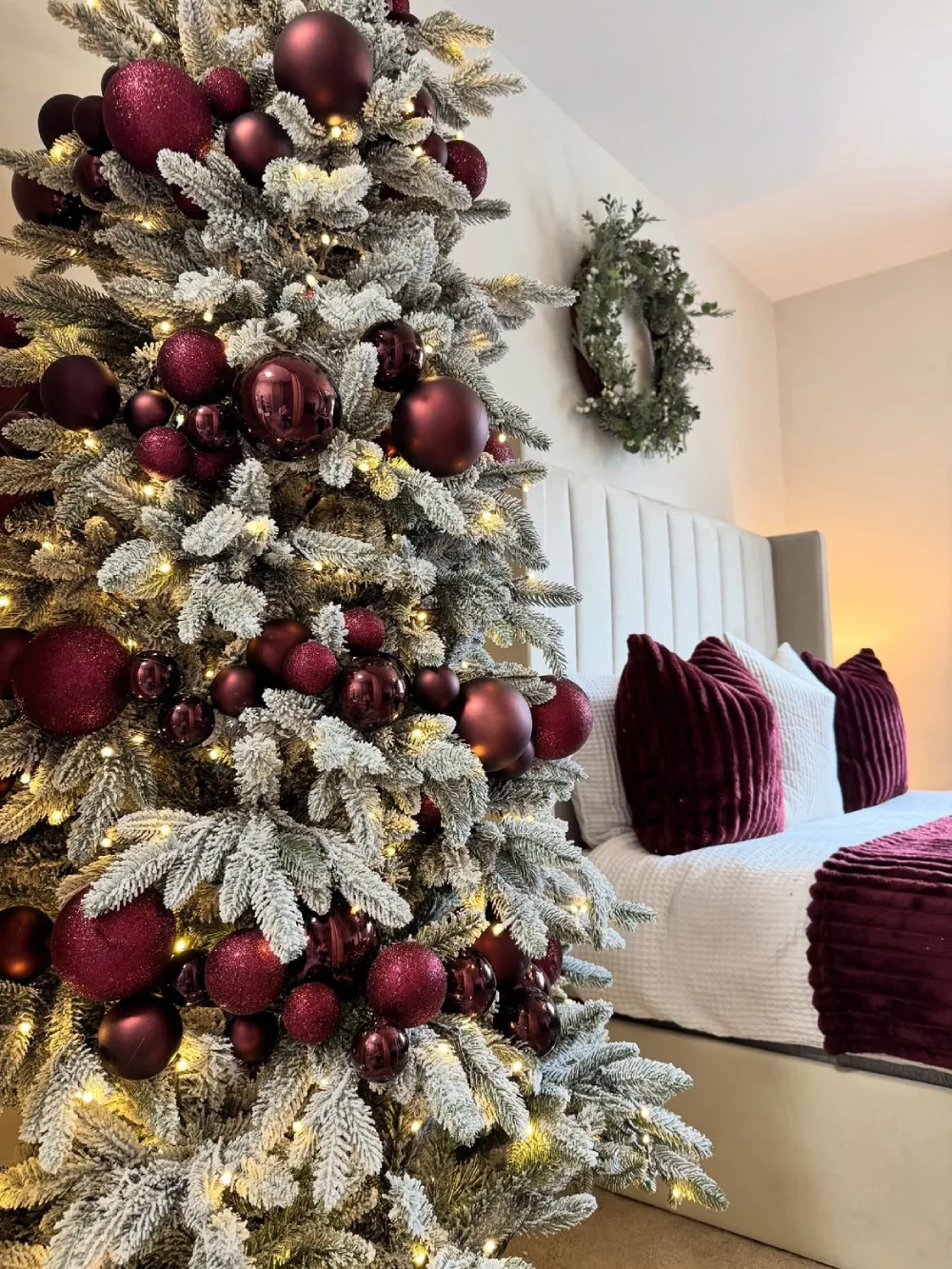 Winter bedroom with burgundy pillows, white bedding, and a flocked Christmas tree