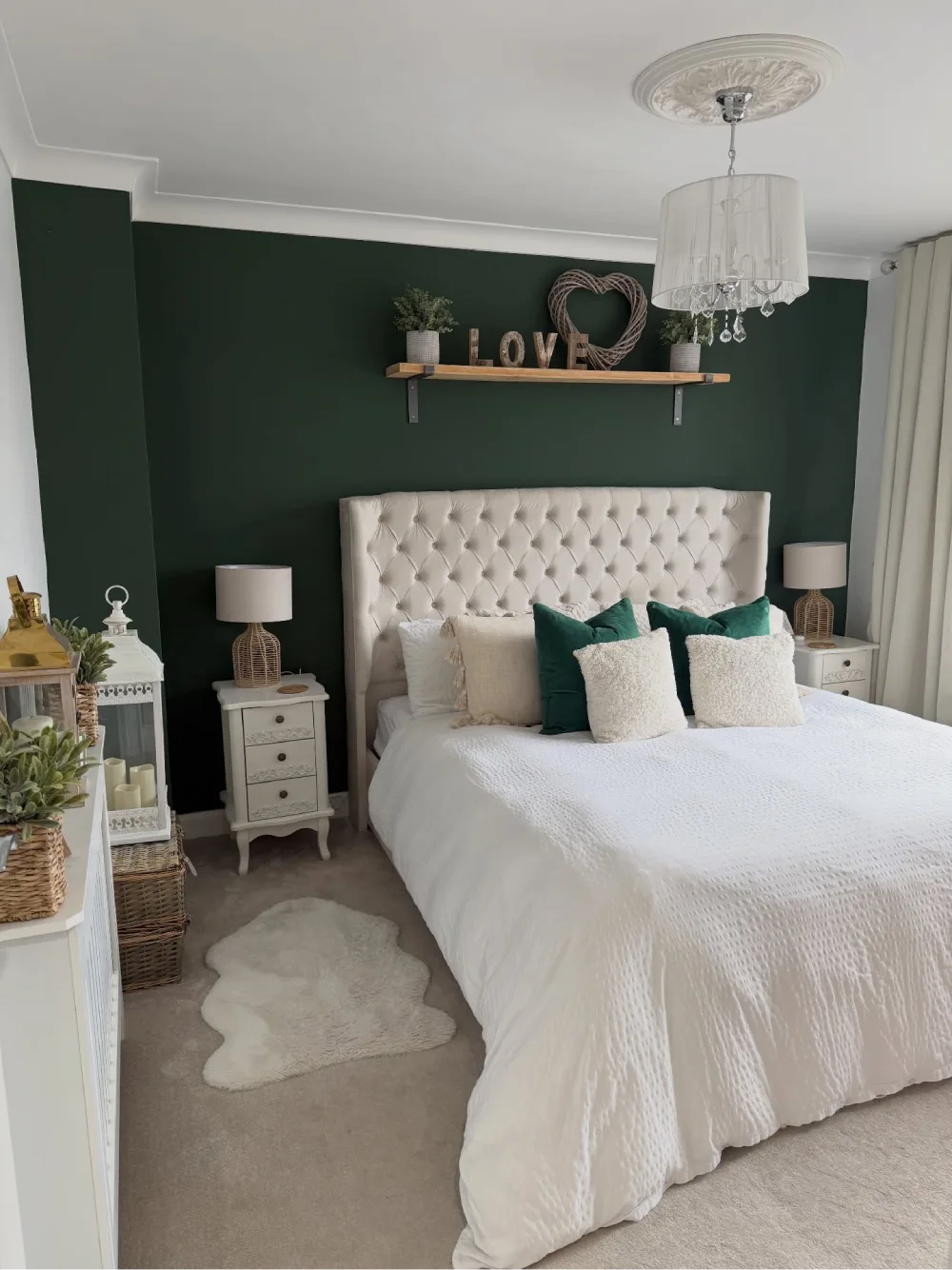 Bedroom with deep forest green walls, white tufted headboard, emerald pillows, woven lamps, and crisp white bedding