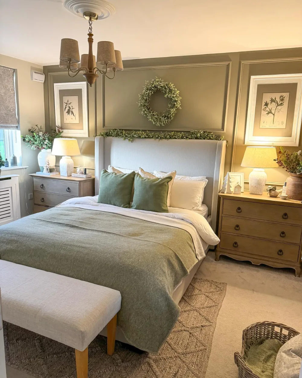 Traditional bedroom with olive green walls, sage bedding, vintage wooden dressers, botanical artwork, and warm bedside lamps