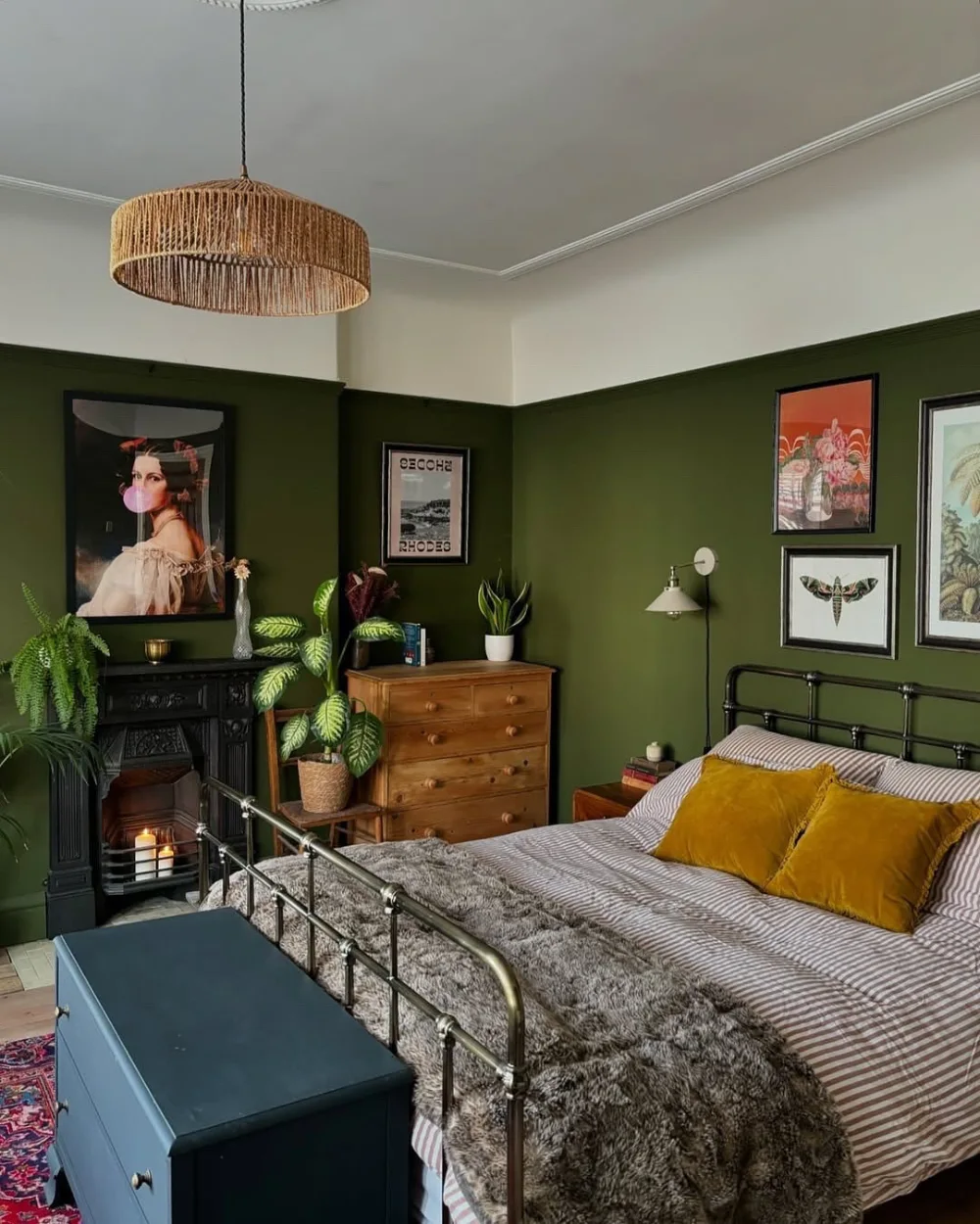 Moody olive green bedroom with vintage artwork, mustard yellow pillows, dark wood furniture, and a brass bed frame