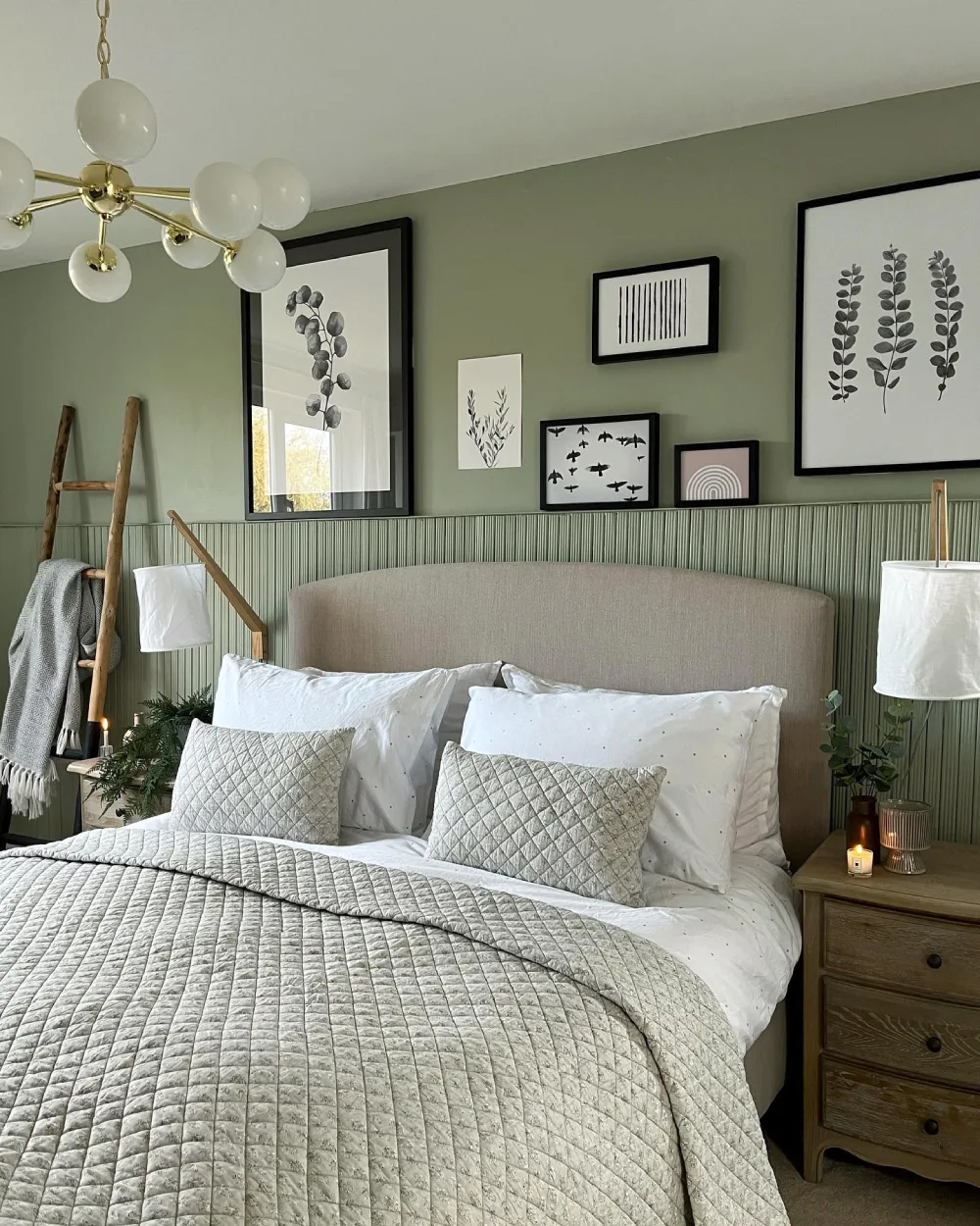 Sage green bedroom with vertical paneling, botanical gallery wall, neutral bedding, and natural wood nightstands