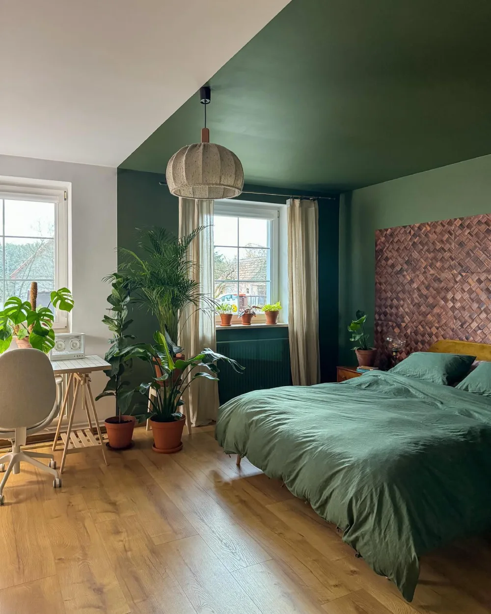 Dramatic bedroom with deep green walls and ceiling, emerald bedding, tropical plants, and woven wood wall decor