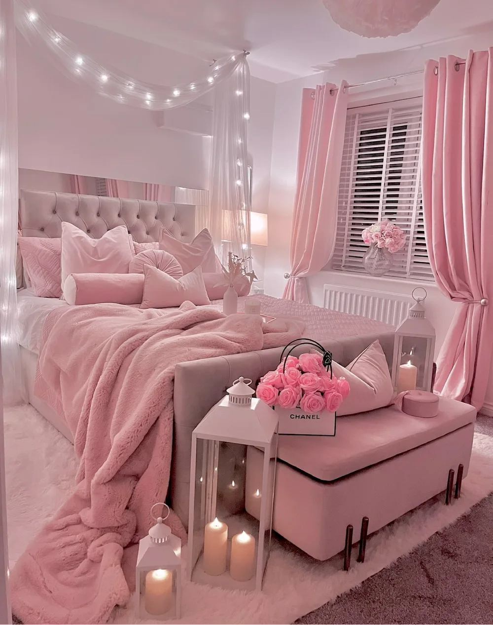 Romantic pink bedroom with a tufted upholstered bed, soft pink curtains, a sheer canopy, plush bedding, and glowing candle lanterns