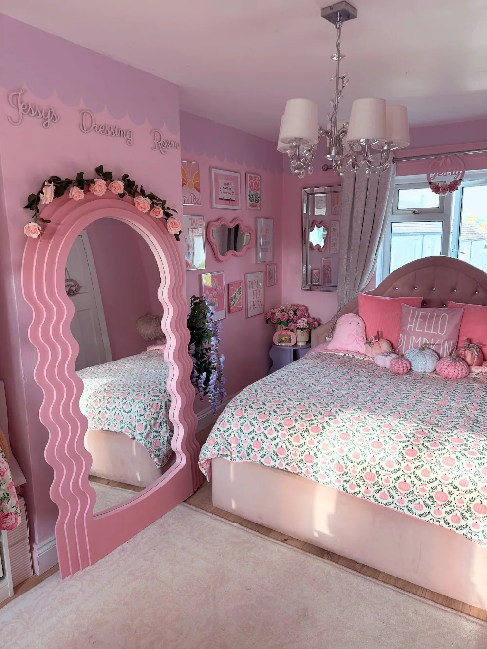 Pink floral bedroom with a wavy full-length mirror, rose-colored walls, patterned bedding, and decorative pink pillows
