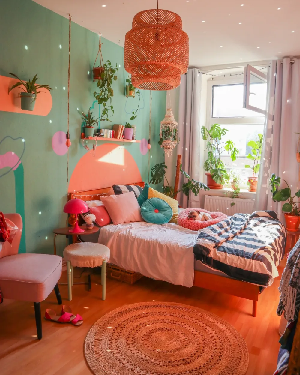Dopamine decor bedroom with a mint green mural, coral pink wall accents, colorful pillows, and a woven pendant light