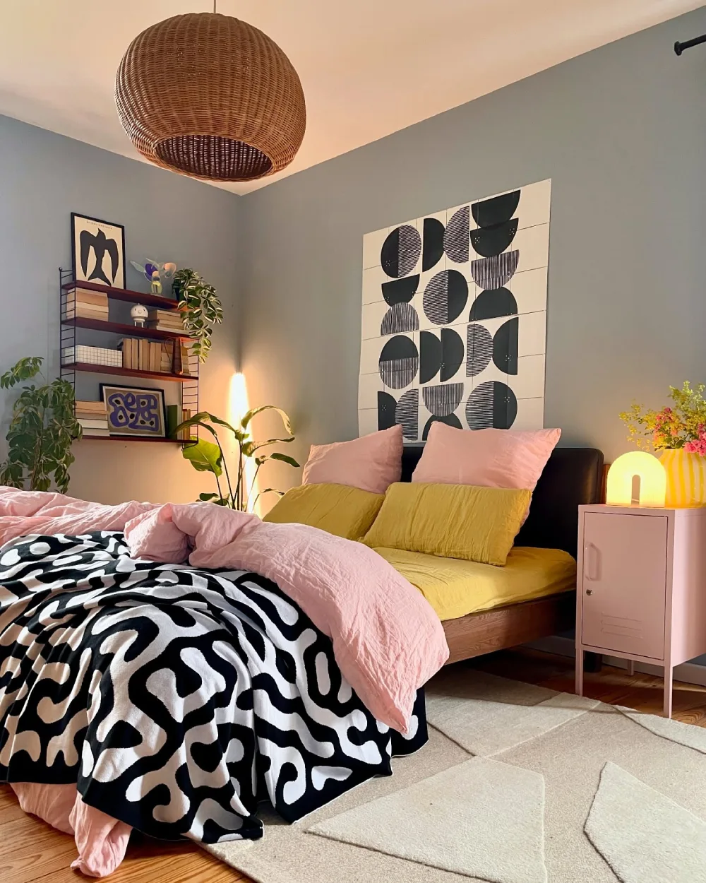 Bedroom with pink and mustard yellow bedding, blue-gray walls, and bold black and white patterns