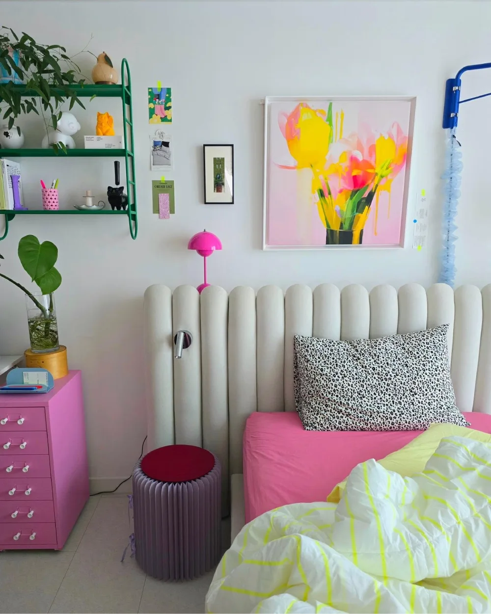Bedroom with hot pink bedding, a white scalloped headboard, green shelves, and colorful artwork