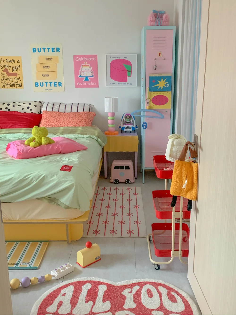Bedroom with mint green bedding, colorful artwork, pastel pink furniture, and red accents