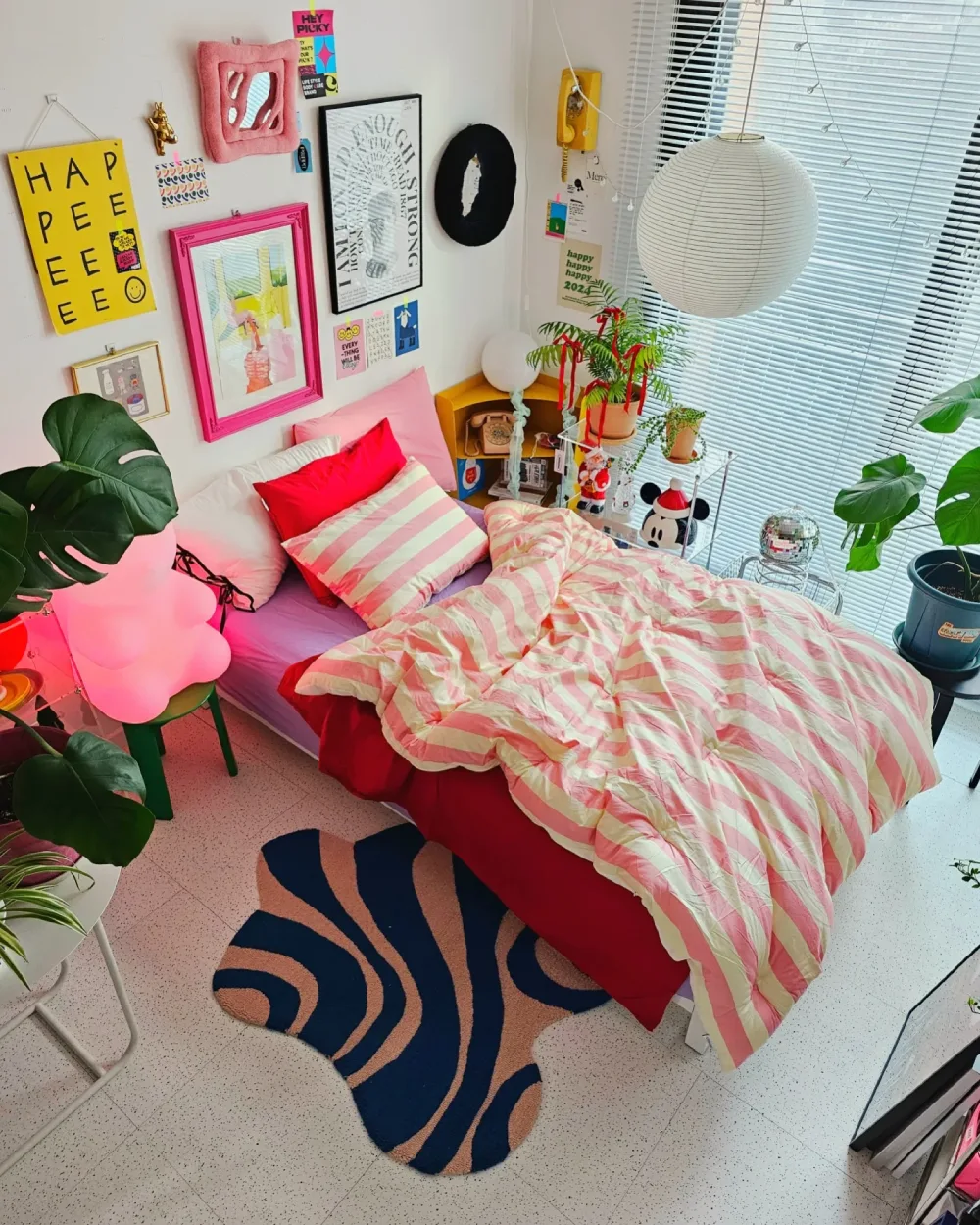 Colorful bedroom with pink striped bedding, red accents, a gallery wall, and green houseplants