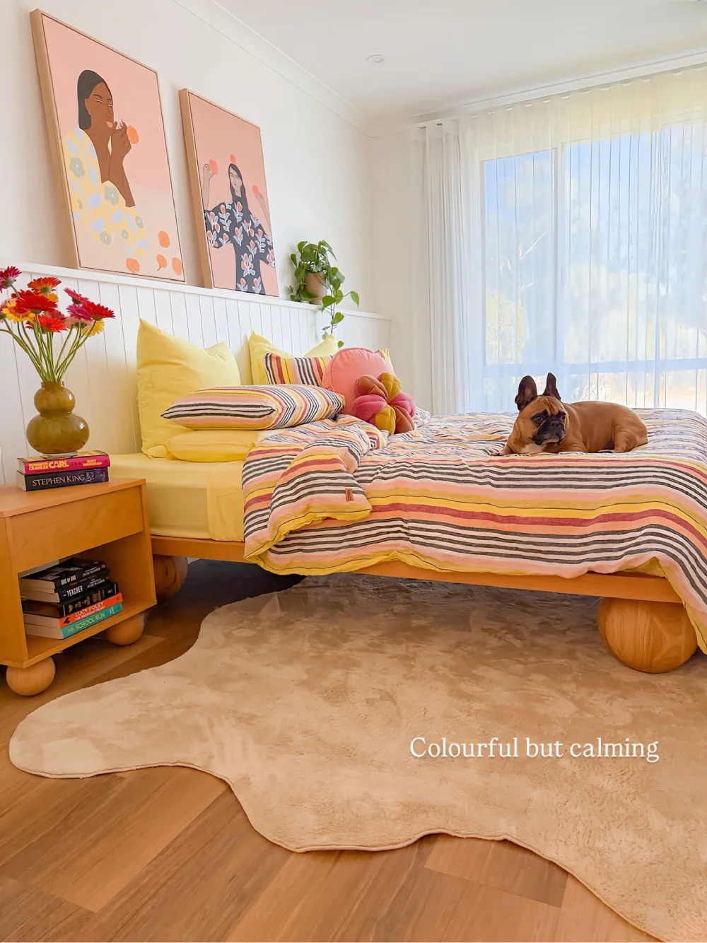 Bedroom with pastel striped bedding, yellow pillows, natural wood furniture, and a soft neutral rug