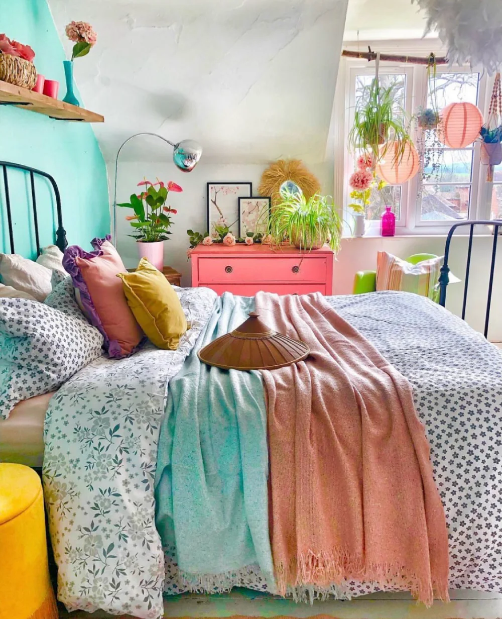Colorful attic bedroom with turquoise walls, coral pink dresser, patterned bedding, pastel pillows, and leafy green plants