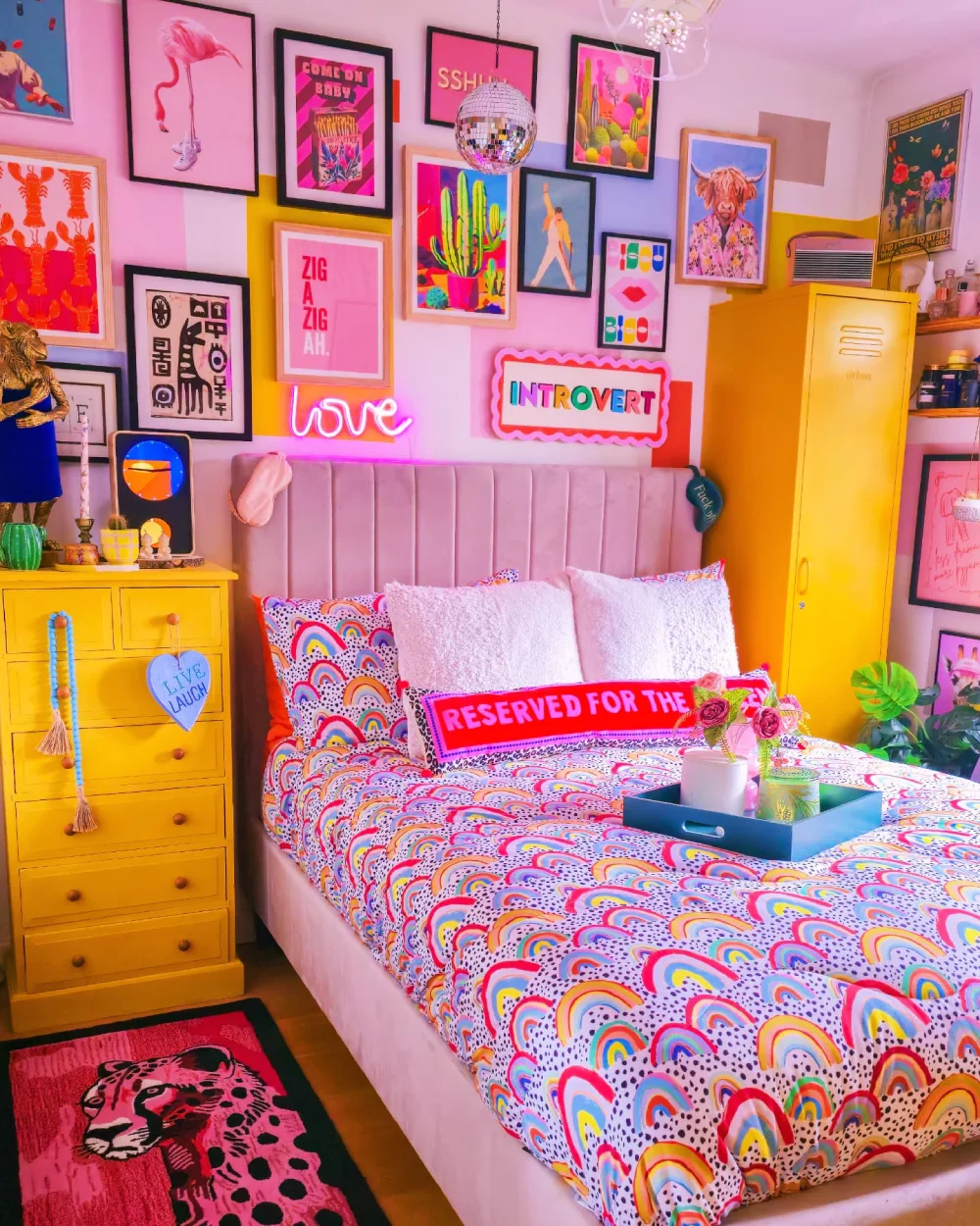 Maximalist bedroom with a pink upholstered headboard, bright yellow furniture, rainbow bedding, and colorful gallery wall