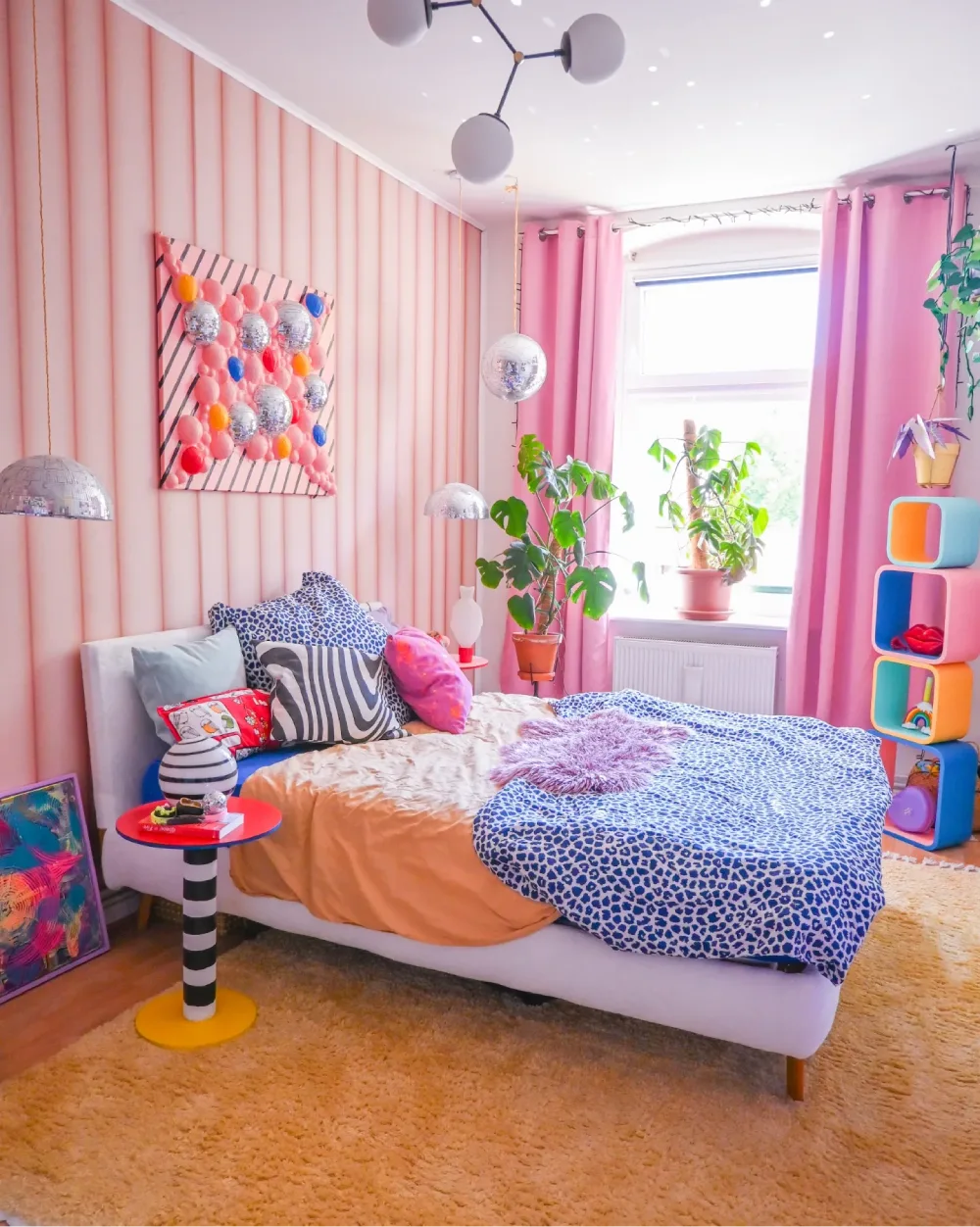 Pink bedroom with vertical blush wall panels, bright pink curtains, leopard print bedding, colorful pillows, and disco ball accents
