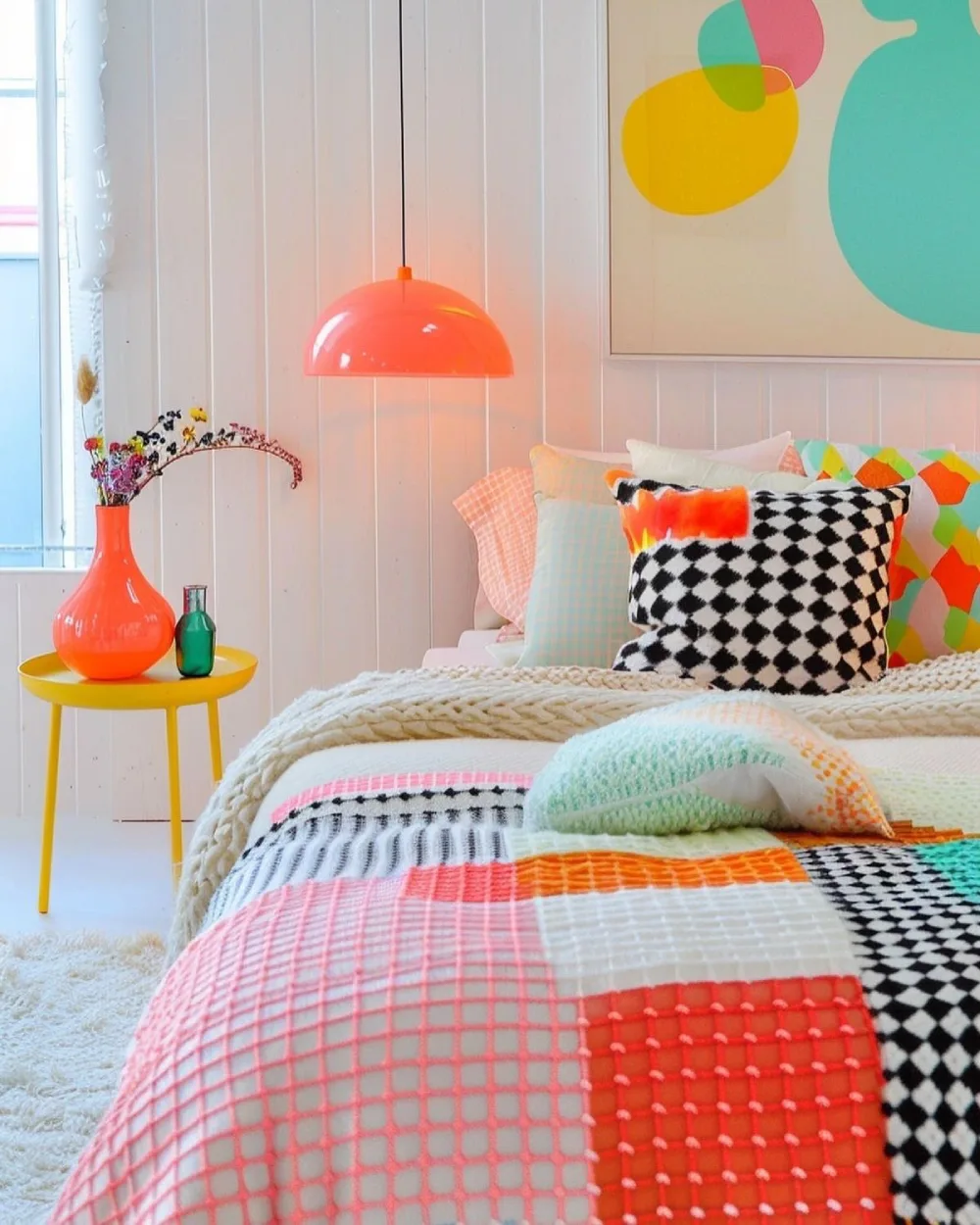 Colorful dopamine decor bedroom with geometric patchwork bedding, a coral pendant light, bright yellow side table, and playful abstract wall art